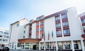 Un hotel de varios pisos con fachada moderna, ventanas amplias y una entrada destacada con zona cubierta.