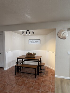 A dining area with a wooden table and benches, a wall-mounted clock, and a framed sign. - WINTER ESCAPE- PET-FRIENDLY 3BD+OFFICE NEAR GOLF COURSES, RIVER AND CASINOS (Mohave Valley)