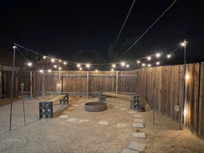 A fenced outdoor area with string lights, benches, a fire pit, and a gravel path. - WINTER ESCAPE- PET-FRIENDLY 3BD+OFFICE NEAR GOLF COURSES, RIVER AND CASINOS (Mohave Valley)