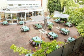 Un patio con mesas y sillas, un edificio con paredes de vidrio y abundante vegetación.