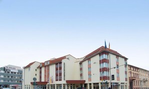 Un hotel de varios pisos con una entrada destacada en esquina, ventanas amplias y un asta de banderín.