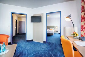 Una camera d'albergo con un letto, una scrivania, una sedia, una televisione e un bagno.