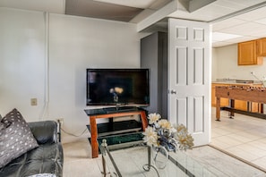 A living room with a flat-screen TV on a wooden stand, a glass coffee table, and a sofa with patterned cushions. - Spacious 5BR Home for Families & Groups (Fort Washington)