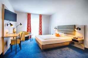 Una camera d'albergo con un letto, una scrivania, una sedia, una televisione e una finestra con tende.