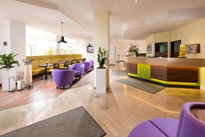Una hall d'albergo con reception, zona salotto con sedute viola e design moderno.