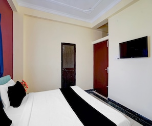 A hotel room with a bed, a wardrobe, a television mounted on the wall, and a door.