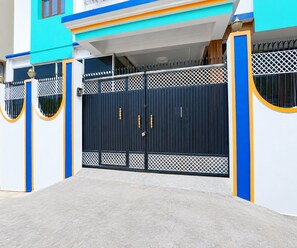 A gated entrance with a blue and white building facade, a concrete driveway, and a metal gate with a keyhole.