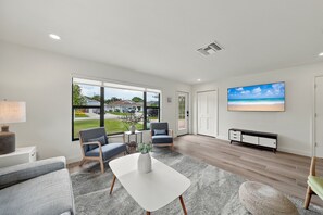 A modern living room with a large window, two chairs, a coffee table, and a flat-screen TV on the wall. - NEW! Cool Breeze - 1 Mile to Vanderbilt Beach! - Heated Pool - Southern Exposure (Naples)