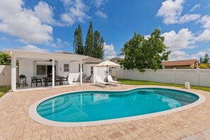 Una piscina amb una zona de porxo coberta, un pati tancat per una tanca i un cel serè.