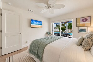 A bedroom with a bed, a ceiling fan, a TV, and a view of an outdoor pool area. - NEW! Cool Breeze - 1 Mile to Vanderbilt Beach! - Heated Pool - Southern Exposure (Naples)