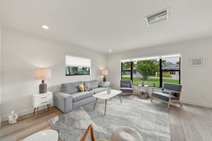 Een moderne woonkamer met een grijze bank, twee fauteuils, een salontafel en een groot raam met uitzicht op het landschap.