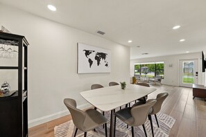 A modern dining area with a marble table, leather chairs, a world map artwork, and a kitchen area with a wine rack. - NEW! Cool Breeze - 1 Mile to Vanderbilt Beach! - Heated Pool - Southern Exposure (Naples)
