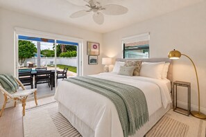 A bedroom with a bed, a bedside table, a lamp, a chair, and a view of an outdoor pool area. - NEW! Cool Breeze - 1 Mile to Vanderbilt Beach! - Heated Pool - Southern Exposure (Naples)
