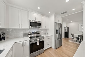 A modern kitchen with white cabinetry, stainless steel appliances, and a tiled backsplash. - NEW! Cool Breeze - 1 Mile to Vanderbilt Beach! - Heated Pool - Southern Exposure (Naples)