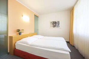 Ein Hotelzimmer mit einem Bett, einem Nachttisch, einer Wandleuchte, einem gerahmten Bild und einem Vorhangfenster.