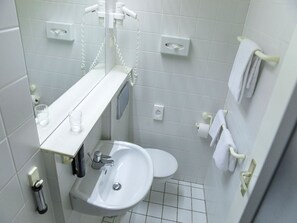 Ein kleines, sauberes Badezimmer mit einem weißen Waschbecken, einer Toilette und einem Spiegel über dem Waschbecken.
