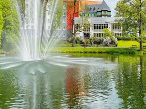 Ein Brunnen in einem Park, im Hintergrund ein Gebäude.