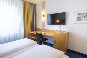 Ein Hotelzimmer mit zwei Betten, einem Schreibtisch, einem Stuhl, einem Fernseher und einem gerahmten Bild an der Wand.