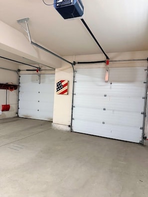 Un garaje con dos puertas cerradas, un proyector instalado en el techo y un objeto rojo en la pared izquierda.