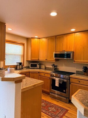 A kitchen with wooden cabinets, a microwave, an oven, and a granite countertop. - Downtown WP Townhome 108 I Private Hot Tub I Great Views I Bunk Room I Discounted Attractions (Winter Park)