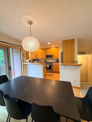 A modern kitchen with a dining area, featuring a large table and chairs, a hanging light fixture, and wooden cabinets. - Downtown WP Townhome 108 I Private Hot Tub I Great Views I Bunk Room I Discounted Attractions (Winter Park)