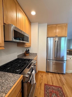 Una cocina con gabinetes de madera, un refrigerador de acero inoxidable, un horno empotrado y una estufa a gas.