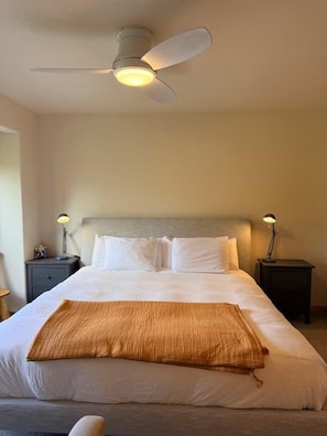 Una habitación de hotel con una cama, ventilador de techo, lámparas de noche y mesita de noche.