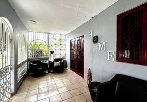 A covered corridor with a tiled floor, a bench, and a door with a red frame. - Huesca House next to Airport (San Juan)