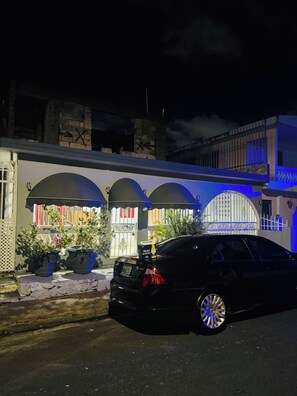 A black car parked in front of a building with a gated entrance and a covered porch area. - Huesca House next to Airport (San Juan)