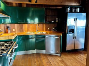 A kitchen with green cabinets, a stainless steel refrigerator, a water dispenser, and a stove.
