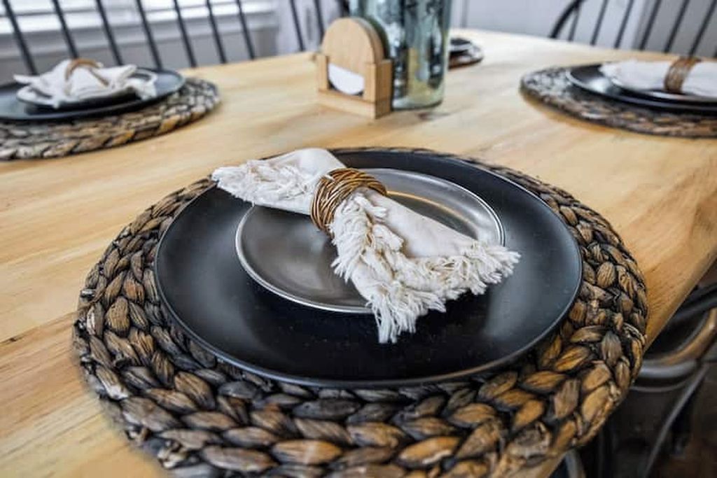 Una mesa con un plato negro, un posavasos tejido y una servilleta blanca atada con un cordón.