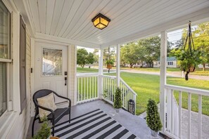 A covered porch with a black chair, a small potted plant, and a hanging planter. - Augusta Retreat Downtown, Medical & Masters (Augusta)