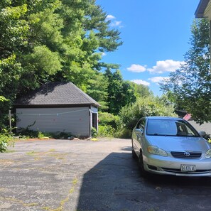 A garage with a car parked in front, surrounded by trees and a clear sky.