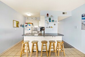 A modern kitchen with a central island, bar stools, and a refrigerator with magnets. - Sunrise Symphony  pool, ocean views, and beach access (Duck)