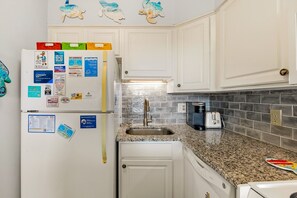 A kitchen with white cabinets, a granite countertop, a stainless steel sink, a toaster, and a coffee maker. - Sunrise Symphony  pool, ocean views, and beach access (Duck)
