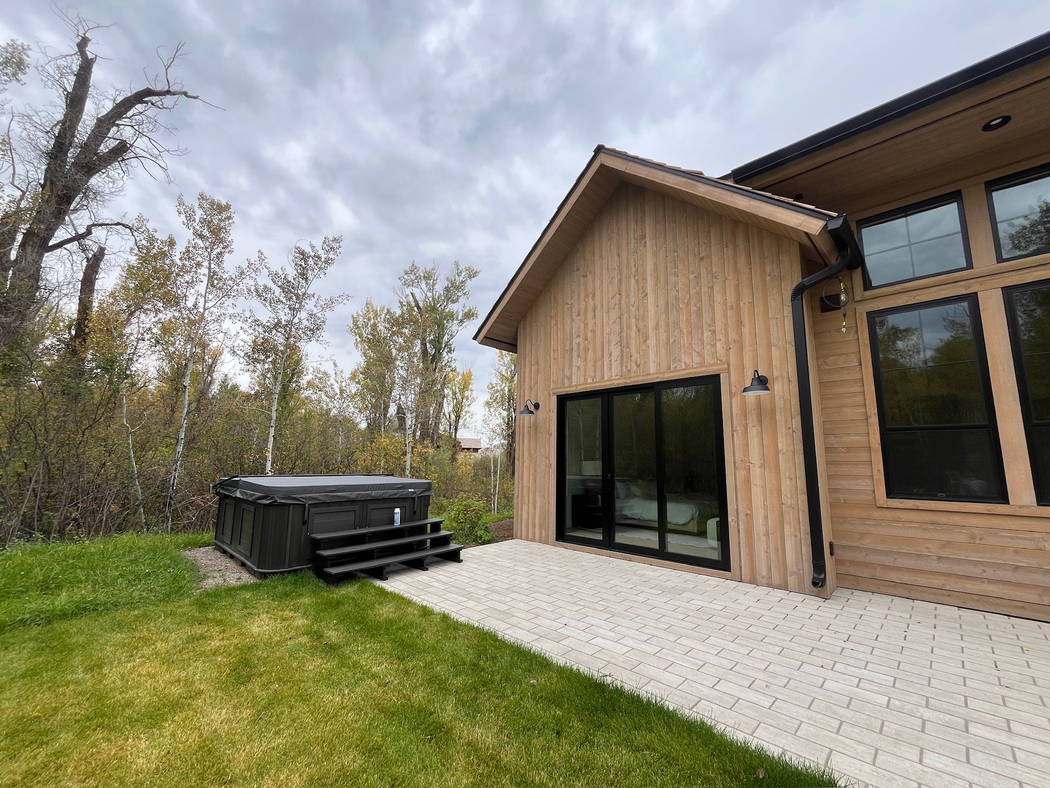 Una moderna casa in legno con vasca idromassaggio, una zona relax esterna coperta e un'ampia porta-finestra in vetro.