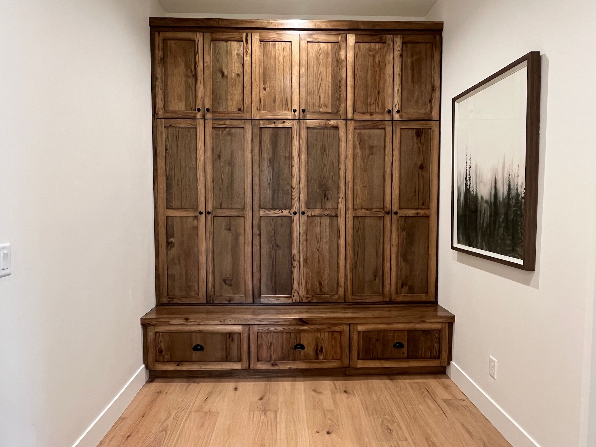 A wooden bench with storage drawers against a wall, a framed picture above it, and a light switch on the wall.