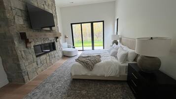 Een moderne slaapkamer met een stenen openhaard, een groot bed met wit beddengoed, uitzicht op het landschap door een schuifdeur en een plafondventilator.