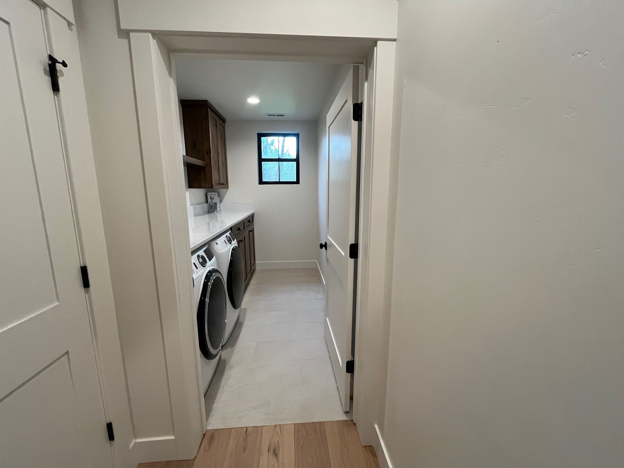 A narrow hallway leading to a laundry area with a washing machine and dryer, wooden cabinets, and a small window.