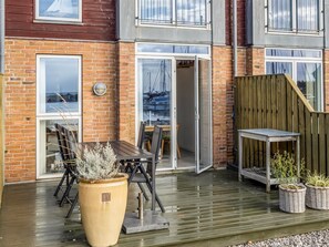 Een patio met een houten terras, een tafel met stoelen, een grote plantenbak en een houten omheining.