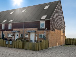 Een woonhuis met twee verdiepingen, een schuin dak, meerdere ramen en een houten omheining.