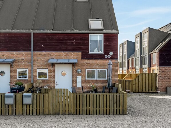 Een woonhuis met twee verdiepingen, gevel van baksteen, houten omheining en een kleine tuin met zitplaatsen.