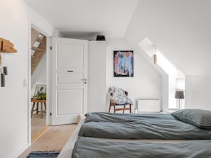 Ein Schlafzimmer mit schrägem Dach, einem Bett, einem Sessel, einem Heizkörper und einem Gemälde.