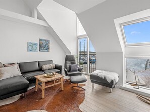 A modern living room with a black leather sofa, a wooden coffee table, and a leather armchair. There are two abstract paintings on the wall, and a large window with a view of the sea and boats. - "Jela" - 10m from the sea by Interhome (Glesborg)