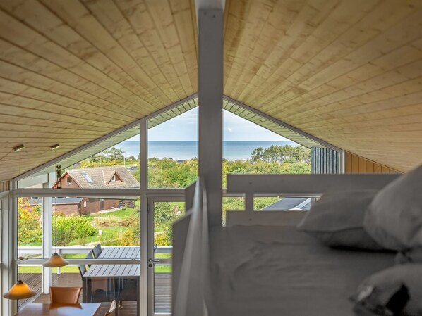 Una habitación con un amplio ventanal con vistas a un paisaje costero, una cama y una mesa con sillas.