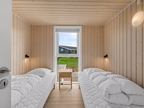 Una habitación con dos camas, una mesita y vista a una casa a través de una puerta.