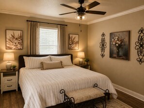 Un dormitorio con cama, mesitas de noche, ventilador de techo y decoración en la pared.