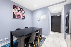 A modern kitchen with a black refrigerator, a dining table with chairs, and a grey wall with a floral painting. - Modern 1-bedroom Apartment in the Heart of Footscray (Melbourne)