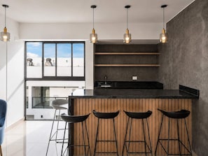 A modern kitchen with a black countertop, wooden bar stools, and pendant lights. - Suite 910 Gym, rooftop y parking (Lima)