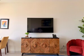 A modern living room with a flat-screen TV mounted on a wooden cabinet, a red armchair, and a potted plant. - 15th Floor Stunning Studio Condo in Sonoran Star (Puerto Peñasco)